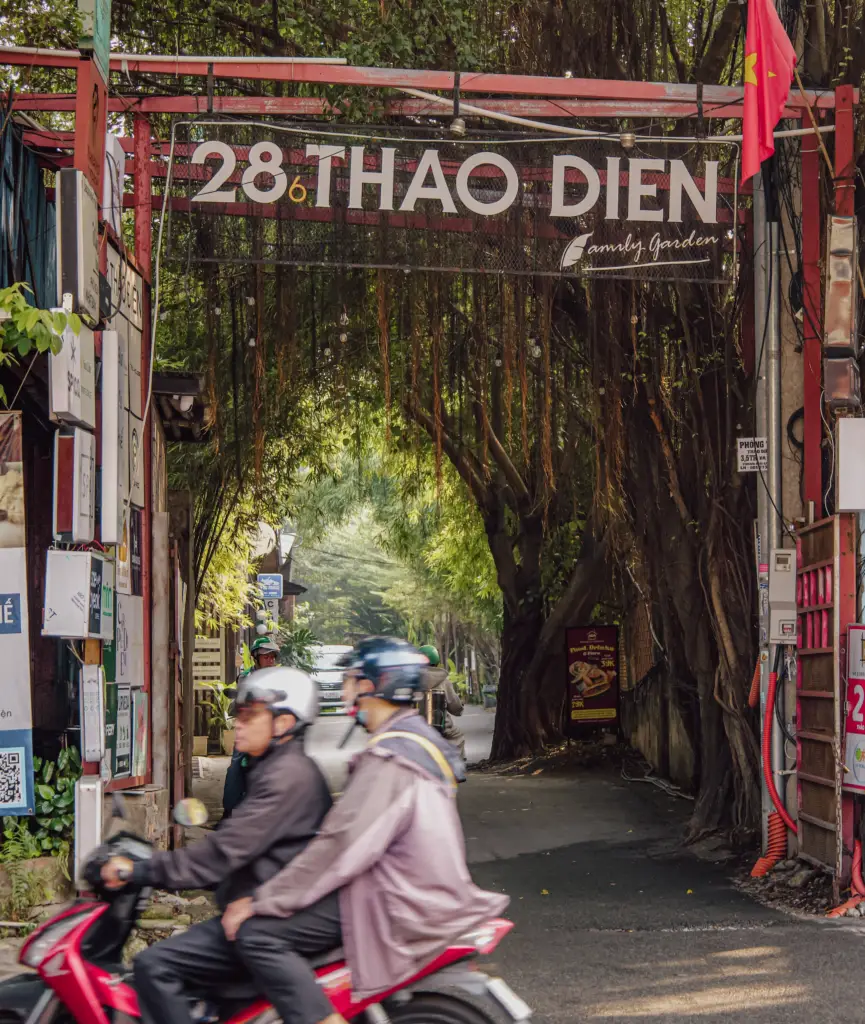Motorbikes passing the tree-lined entrance to 28/6 Thảo Điền